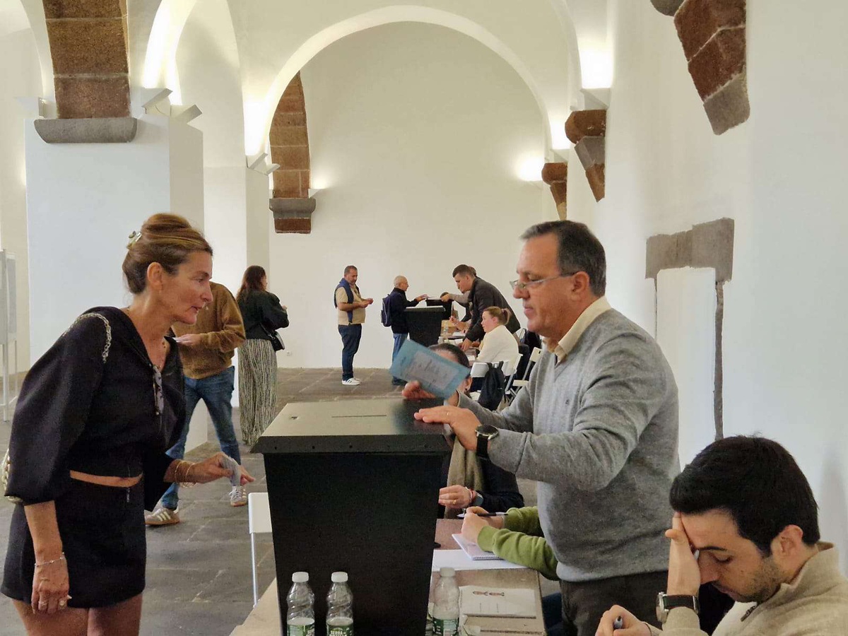 Carlos Caldeira (à direita) auxilia uma eleitora no momento de depositar o voto na urna.